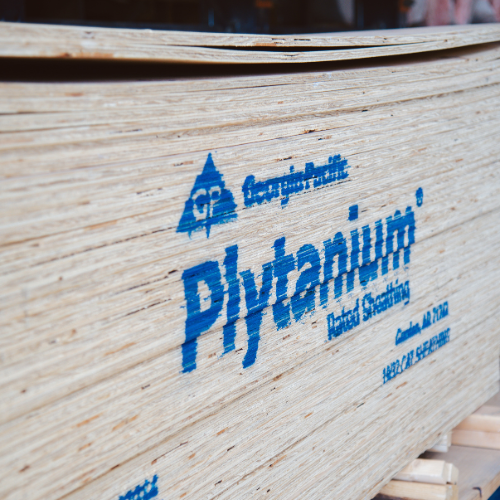 Stack of plywood sheets with “Plytanium” printed in blue on the side. The texture of the wood is visible, suggesting a construction setting.