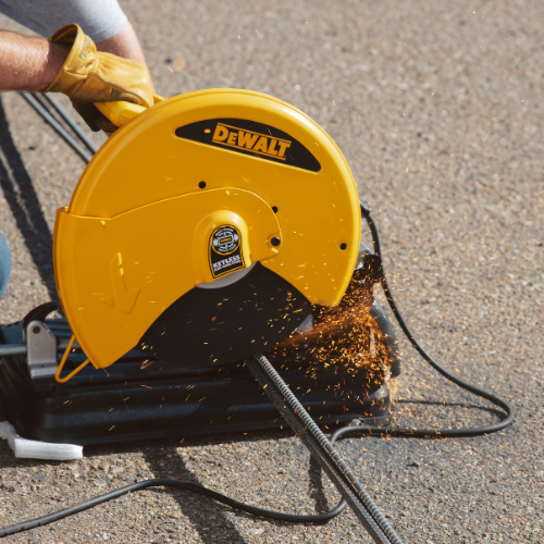 A person using a yellow DeWalt chop saw cuts through a metal rod on concrete, creating bright sparks. The scene conveys a sense of focus and precision.