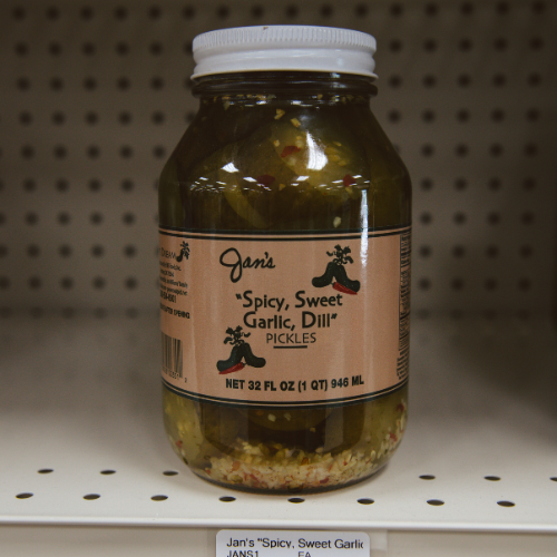 A jar of "Jan's Spicy, Sweet Garlic, Dill Pickles" on a store shelf. The label features chili peppers, emphasizing a spicy flavor.