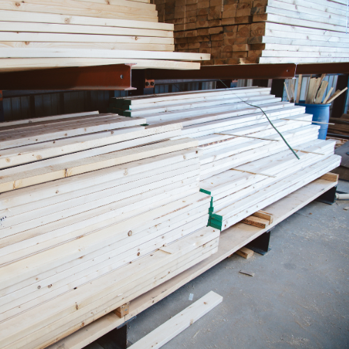 Stacked wooden planks in a warehouse, neatly arranged on metal shelves. The setting is industrial, conveying organization and readiness for use.
