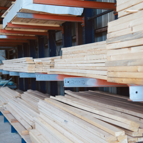 Stacks of lumber neatly arranged on metal shelves in a warehouse. The wood planks vary in size, creating an organized, industrial atmosphere.