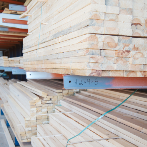 Stacks of wooden planks labeled "2x4x8" on metal shelves in a warehouse. The wood is neatly arranged, creating a sense of order and efficiency.
