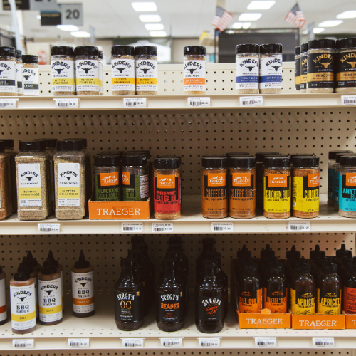 Store shelf displaying various seasoning bottles and barbecue sauces in vibrant packaging. Products are neatly arranged, evoking a sense of variety and choice.