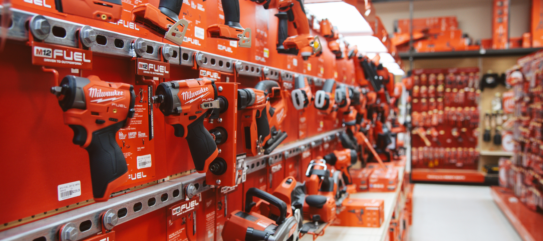 Store aisle displaying various Milwaukee power tools on bright red shelves. The tools, prominently featuring drills, convey a sense of efficiency and professionalism.